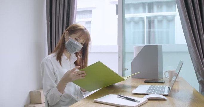 Asian woman wearing mask working from home stressed deadline quarantine workplace desk with computer and protective sanitizer, hand gel alcohol clean wash, Prevent the spread of coronavirus.