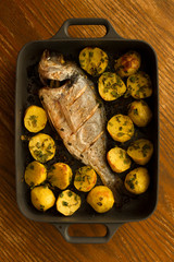 dorado roasted with potato in a black tray on wooden background