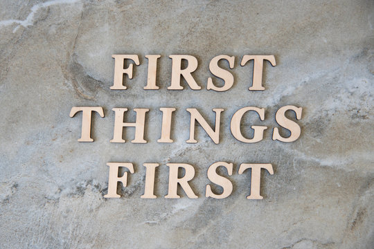 first things first , writen wooden letters on stone background