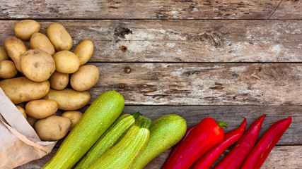 Raw organic red pepper, zucchine and potatoes spilling out of a recycled paper bag onto natural weathered wooden boards. Copy space.
