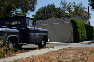 Old rusty black truck, parked on the street in front of a white house.
