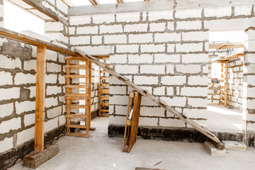 Building site of a house under construction. Unfinished house walls made from white aerated autoclaved concrete blocks. Scaffolding for workers assembled from boards and Euro-pallets.