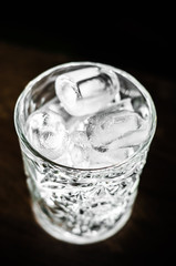 Ice cubes in an empty glass on a dark background, front view with details
