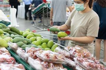 Asian woman wear a face mask,chooses necessary food,mango,fruit while shopping at supermarket,people panic buying, hoarding during the Covid-19,Coronavirus spread,girl preparing for pandemic,stay home