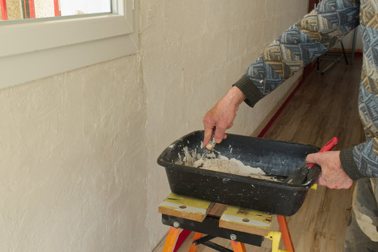 D&eacute;pose d'enduit, de pl&acirc;tre sur un mur par un pl&acirc;trier et pr&eacute;paration du m&eacute;lange dans une auge pour boucher et lisser l'enduit sur la paroi &agrave; l'aide d'un couteau et d'une spatule