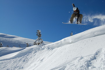 Snowboarder in action on a sunny winter day.  High jump from the hill followed by snow powder....