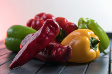 Composition of peppers of three different colors. Bright colors of vegetables. Juicy fresh peppers on a dark wooden table. Red, yellow, and green.