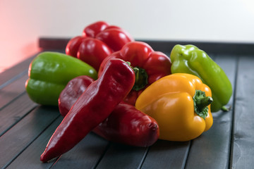 Composition of peppers of three different colors. Bright colors of vegetables. Juicy fresh peppers on a dark wooden table. Red, yellow, and green.