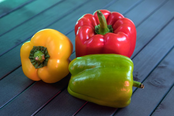 Composition of peppers of three different colors. Bright colors of vegetables. Juicy fresh peppers on a dark wooden table. Red, yellow, and green.
