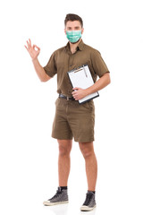Courier wearing face mask is holding a clipboard under the arm and showing ok hand sign