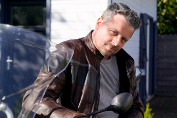 Fototapeta na wymiar handsome beard man in brown motorbike fashion jacket sit on motorcycle outdoors