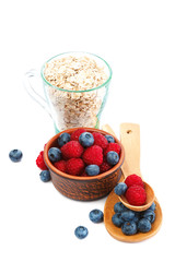 Fresh blueberries and raspberries, oatmeal in a bowl with a wooden spoon