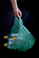 hand holding green plastic bag with empty plastic bottles on dark background, stop plastic, zero weist