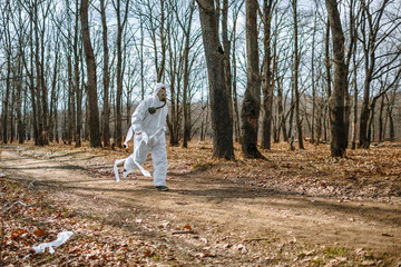 Fototapeta premium A man in a sanitary suit and a gas mask is Jogging in the woods. The suit is tied with toilet paper