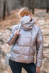 A girl in a sanitary mask and a shiny jacket stands in the woods