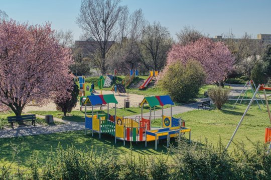 pusty plac zabaw dla dzieci podczas pandemii, zakaz poruszania się podczas pandemii, kwitnące kolorowe krzaki, przyrządy do zabaw i ćwiczeń