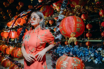 A beautiful asian woman on modern Chinese traditional dress standing at front of red lantern for Chinese new year.