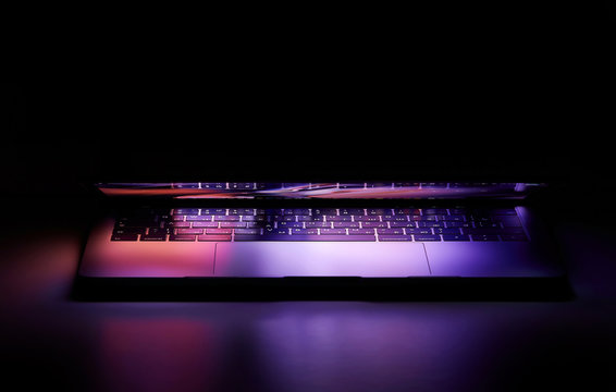 Laptop with Touchbar on dark background, purple light