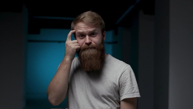 30s Mad Disappointed Bearded Youthful Redhead Guy Tapping on his Head in Anger. Impatient Millennial Male with Negative Attitude Showing Stress Problem and Headache in a Dark Room Contemporary Concept