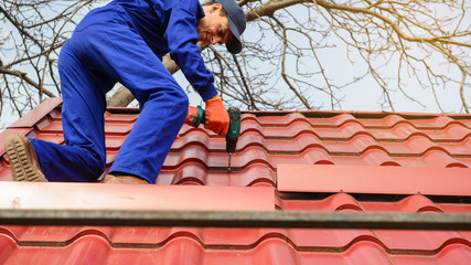 Young man worker in blue overall fix a metal tile roof