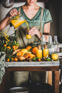 Immune boosting vitamin health defending drink. Young woman pouring fresh turmeric, ginger, citrus juice shot from jug to bottle in kitchen. Pure vegan Immunity system booster