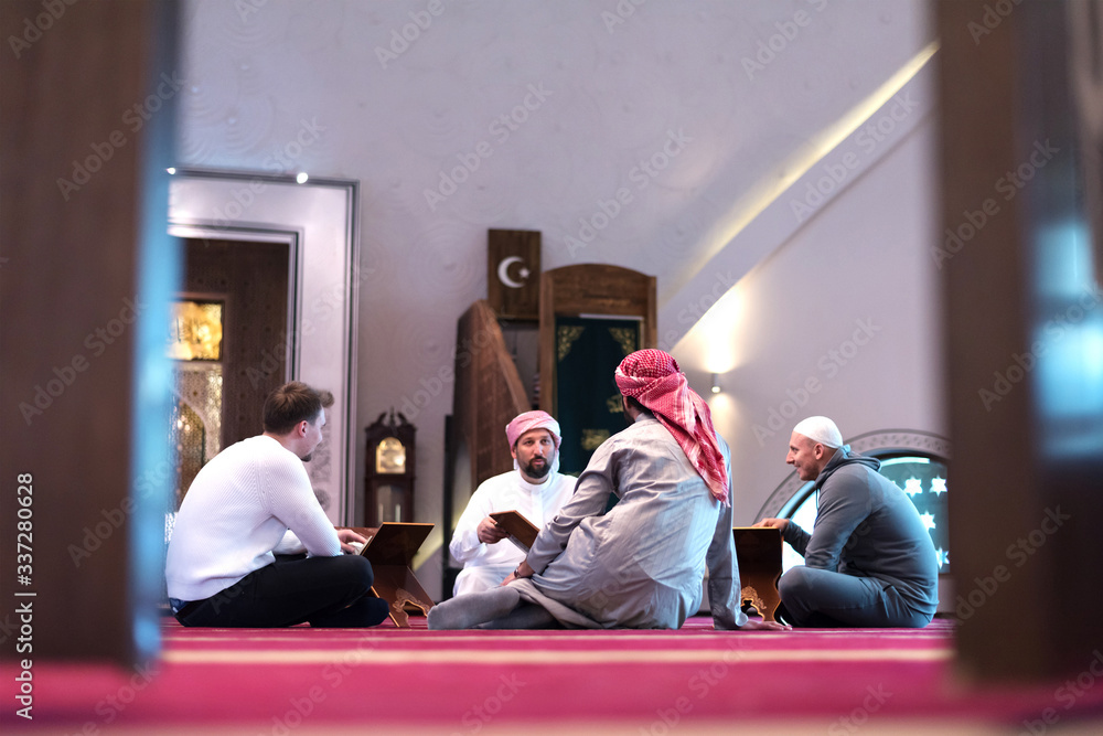 Wall mural group of muliethnic religious muslim young people praying and reading koran together. group of musli