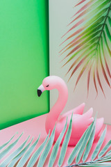 Plastic flamingo in the pink and green corner with palm leaves. Hot summer vacation concept in tropical style.