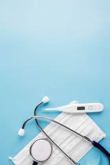 Composition with medical stethoscope, disposable face masks, thermometer and pills on a blue background. Top view. Free copy space.