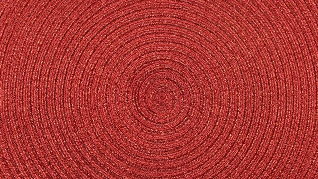 The braided mat spins on the stand. View from above. The texture of the fabric. Red wicker fabric. Close-up. Can be used as a background.
