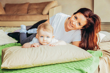 Fototapeta na wymiar Stay Home Stay Safe. Young mother holding her child. Woman and infant little girl relaxing in white light bedroom indoors. Happy family at home. Young mom playing whith her daughter.