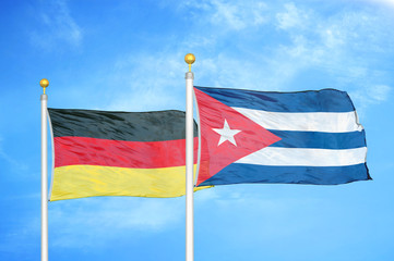 Germany and Cuba two flags on flagpoles and blue cloudy sky