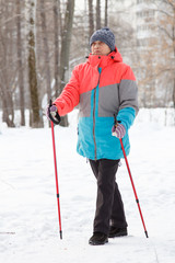 elderly woman in a winter park holding ski poles in her hands doing Nordic Walking. Winter sport. Activity of retirees.