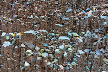 Layer of soil, or a wall of soil, with many blue rocks around the dark soil, close up.