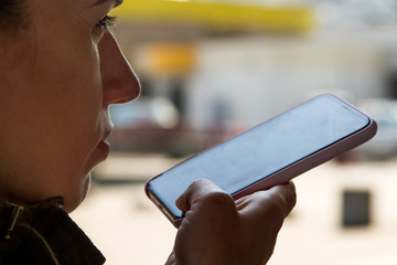 A woman uses a voice assistant in her smartphone, dictating speech using speech recognition...