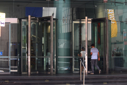 Revolving door entrance to glass modern office building in the city. Pictured are two people walking though the glass doors. 135 King street, Sydney