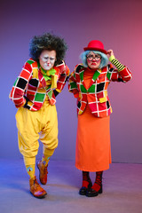 Two clowns a man and a woman with makeup in bright colored costumes are fooling around and showing a presentation