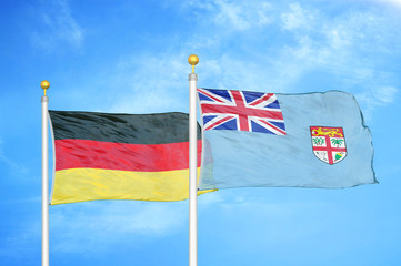 Germany and Fiji two flags on flagpoles and blue cloudy sky