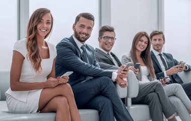 business people with mobile phones sitting in the bright hall