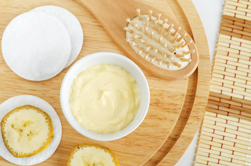 Diy banana and yogurt mask (face cream) in the small white bowl, wooden hair brush, cotton pads and...