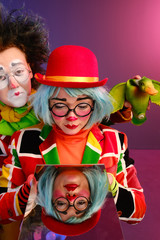 two clowns a man and a woman with bright makeup in colored costumes say they look at their reflection in the mirror. 