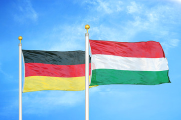 Germany and Hungary two flags on flagpoles and blue cloudy sky
