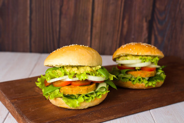 vegetarian hamburger with lentil cutlet, avocado, tomatoes, onions, lettuce on a wooden table on a dark background. delicious Burger for vegetarians