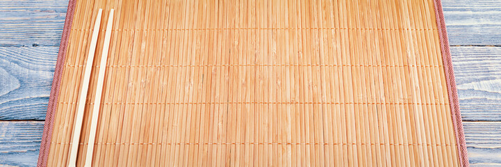 Two wooden chopsticks on a bamboo mat