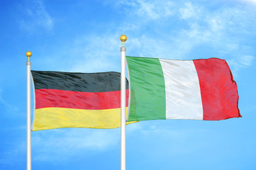 Germany and Italy two flags on flagpoles and blue cloudy sky