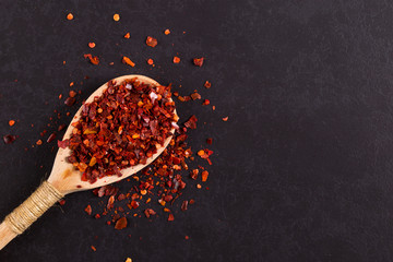 Crushed dried chili peppers in a wooden spoon scattered on a black background. Concept, copy space.