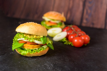 vegetarian hamburger with lentil cutlet, avocado, tomatoes, onions, lettuce on a wooden table on a dark background. delicious Burger for vegetarians. close up