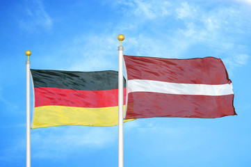 Germany and Latvia two flags on flagpoles and blue cloudy sky
