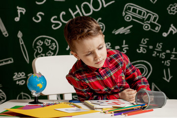 Emotional school boy sitting on the desk with many school supplies. First day of school. Kid boy from primary school. Back to school. Child from elementary school.