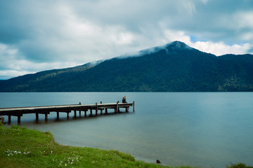 Kaniere Lake, New Zealand, October 7, 2019: Beautiful view of a European woman sitting at the end of the pier admiring the scenery