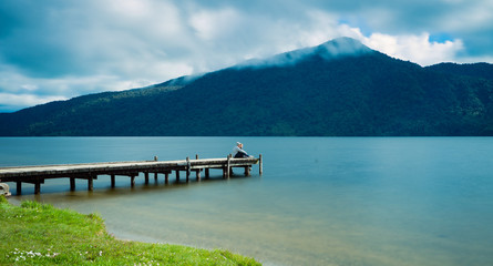 Kaniere Lake, New Zealand, October 7, 2019: Beautiful panorama of a loving couple sitting at the end of the pier admiring the landscape